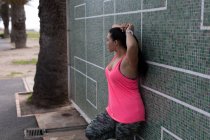 Vue latérale du joggeur féminin appuyé contre le mur — Photo de stock