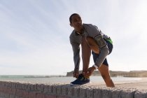 Чоловік-спортсмен зав'язує свої шнурки на навколишній стіні на пляжі — стокове фото