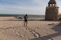Мужской спортсмен проверяет время на своих умных часах во время пробежки возле пляжа — стоковое фото