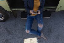 Unterteil der Frau benutzt Handy und sitzt auf offener Transportertür — Stockfoto