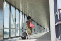 Вид ззаду жінки з багажною сумкою, що йде в аеропорту — стокове фото