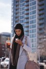 Hijab-Frau trinkt kalten Kaffee, während sie ihr Handy in der Stadt benutzt — Stockfoto