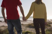 Средняя часть пары, держащихся за руки и стоящих на пляже — стоковое фото