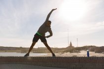 Atleta masculino exercitando na parede circundante perto da praia — Fotografia de Stock