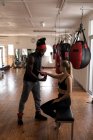 Male trainer assisting female boxer in wearing hand wrap in fitness studio — Stock Photo