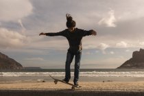 Junger Mann skateboardet auf Mauer am Strand — Stockfoto