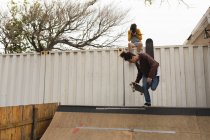 Giovane skateboarder femminile cliccando foto mentre skateboarder maschile pattinaggio sulla rampa di skateboard — Foto stock