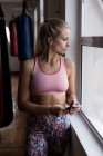 Задумчивая женщина-боксер с помощью мобильного телефона в фитнес-студии — стоковое фото