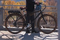Sección baja del hombre de pie con bicicleta en el puente de la ciudad - foto de stock