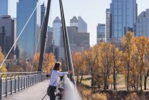 Homem atencioso de pé com bicicleta na ponte da cidade — Fotografia de Stock
