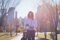 Uomo che utilizza il telefono cellulare mentre cammina con la bicicletta per strada in città — Foto stock