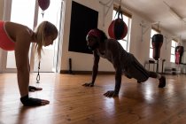 Male trainer assisting female boxer in doing push ups in fitness studio — Stock Photo