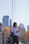 Homem usando telefone celular enquanto toma café na ponte da cidade — Fotografia de Stock