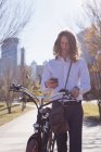 Uomo che utilizza il telefono cellulare mentre cammina con la bicicletta per strada in città — Foto stock