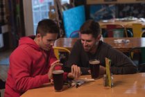 Friends discussing on mobile phone at table in pub — Stock Photo