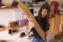 Schöne Frau untersucht Skateboard-Deck in Werkstatt — Stockfoto