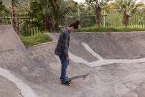 Вид сбоку на человека, стоящего с скейтбордом в скейт-парке — стоковое фото