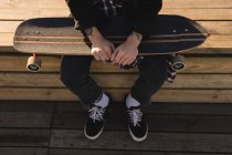 Low section of skateboarder sitting with skateboard on wooden bench — Stock Photo