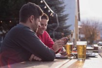 Amigos discutindo no celular enquanto bebem no pub ao ar livre — Fotografia de Stock