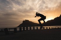Silhouette di skateboarder skateboard vicino alla spiaggia durante il tramonto — Foto stock