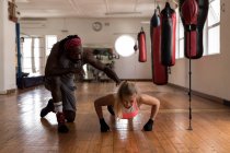 Entrenador masculino que ayuda a la boxeadora femenina a hacer flexiones en el gimnasio - foto de stock