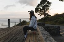 Боковой вид женщины-скейтбордистки, сидящей на скейтборде за перилами в наблюдательном пункте — стоковое фото