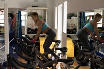 Boxeadora haciendo ejercicio en bicicleta estática en gimnasio - foto de stock