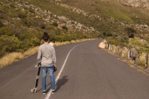 Rear view of skateboarder standing with skateboard on downhill — Stock Photo