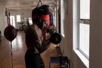 Vista lateral do boxeador masculino exercitando com barra no estúdio de fitness — Fotografia de Stock