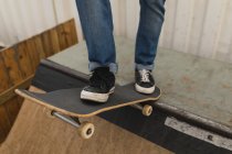 Low section of skateboarder standing with skateboard on skateboard ramp at skateboard court — Stock Photo