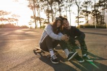 Feliz casal skatista tomando selfie no celular na estrada de campo — Fotografia de Stock