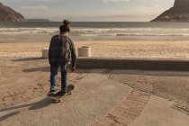 Вид сзади на скейтбординг на пляже — стоковое фото