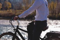 Средняя часть человека отдыхает на велосипеде возле реки — стоковое фото