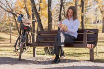 Jovem tomando café enquanto sentado em um banco no parque — Fotografia de Stock