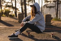 Ragionevole skateboarder femminile seduto su skateboard su strada di campagna — Foto stock