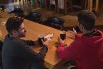Amigos hablando entre sí mientras toman cerveza en el mostrador en el pub - foto de stock