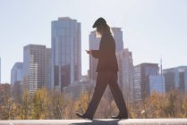 Hombre usando el teléfono móvil mientras camina por una carretera en la ciudad - foto de stock