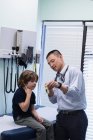 Front view of young asian male doctor showing ear model to caucasian boy patient in clinic — Stock Photo