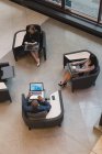 Vista superior de pessoas de negócios usando dispositivos multimídia sentados nas poltronas no lobby no escritório — Fotografia de Stock
