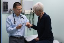 Молоді азіатські чоловічого лікар вимірювання рівня цукру крові з глюкометрії старший жінка в клініці — стокове фото