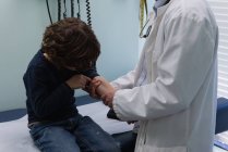 Section médiane du jeune médecin masculin asiatique vérifiant la pression artérielle du patient garçon caucasien en clinique — Photo de stock