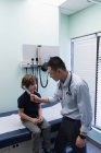 Вид збоку молоді азіатські чоловічого лікар показ камертон до кавказька хлопчик пацієнта в клініку — стокове фото