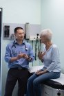 Молоді азіатські чоловічого лікар і старший пацієнта обговоренню над серцем модель в клініці — стокове фото