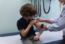 Вид сбоку на молодого врача-азиата, вводящего шприц кавказскому мальчику в клинику — стоковое фото