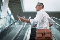 Side view of businessman checking his mobile phone on the escalator in office — Stock Photo