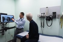 Vista trasera del joven médico asiático discutiendo sobre el informe de rayos X en la computadora en la clínica - foto de stock