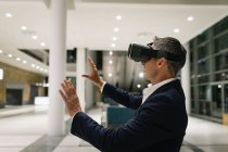 Side view of a businessman experiencing VR headset and raising his hands in the corridor in office by night — Stock Photo