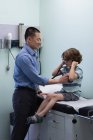 Side view of young asian male doctor examining caucasian boy patient with stethoscope in clinic — Stock Photo