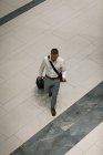 Підвищений вигляд бізнесмена з подорожньою валізою, який дивиться на свій смартфон під час ходьби в коридорі — стокове фото