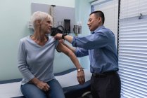 Joven asiático médico masculino inyectando paciente senior en la clínica - foto de stock